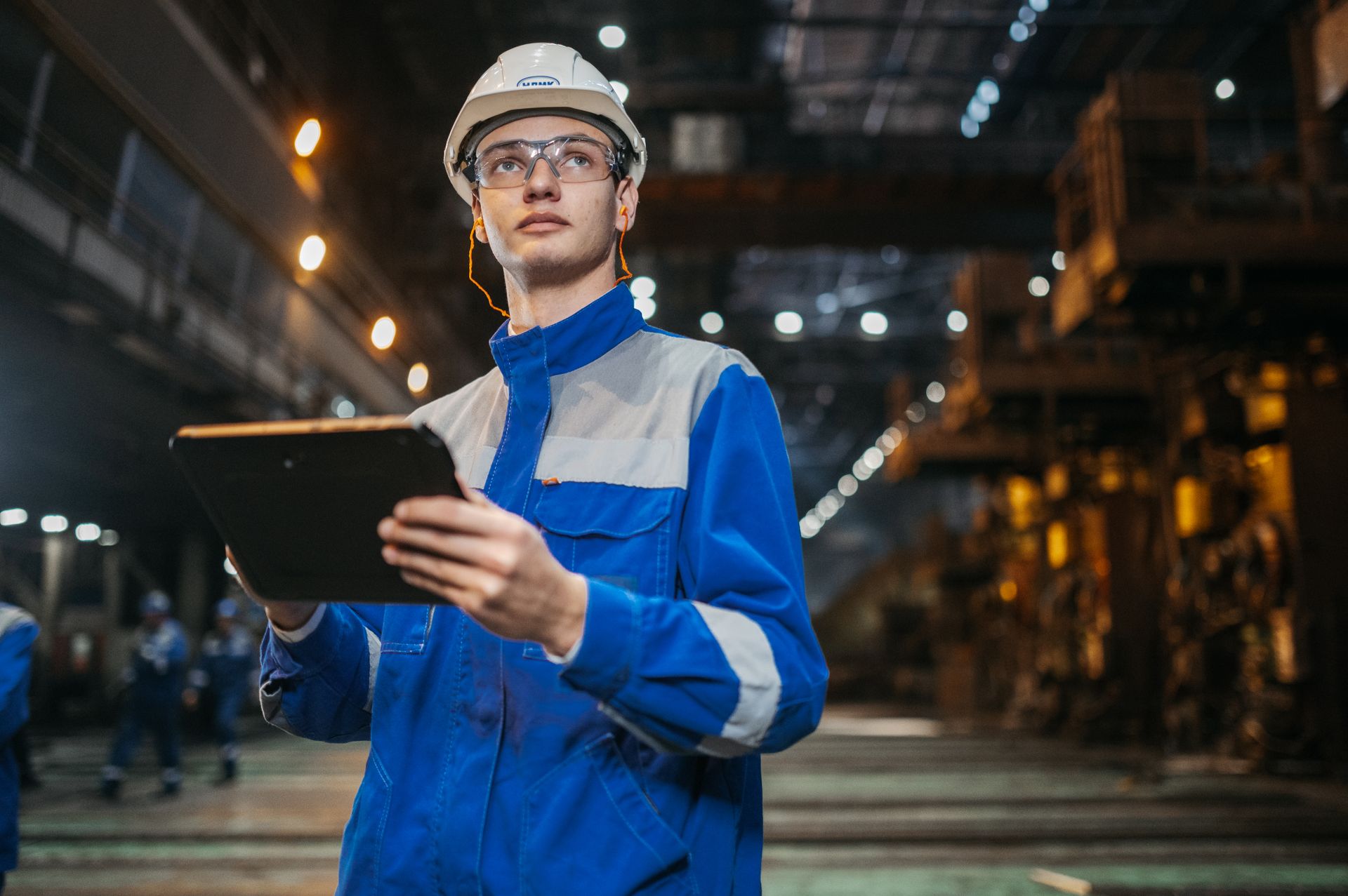 Automation engineer in helmet and safety glasses reviewing plant data on a tablet