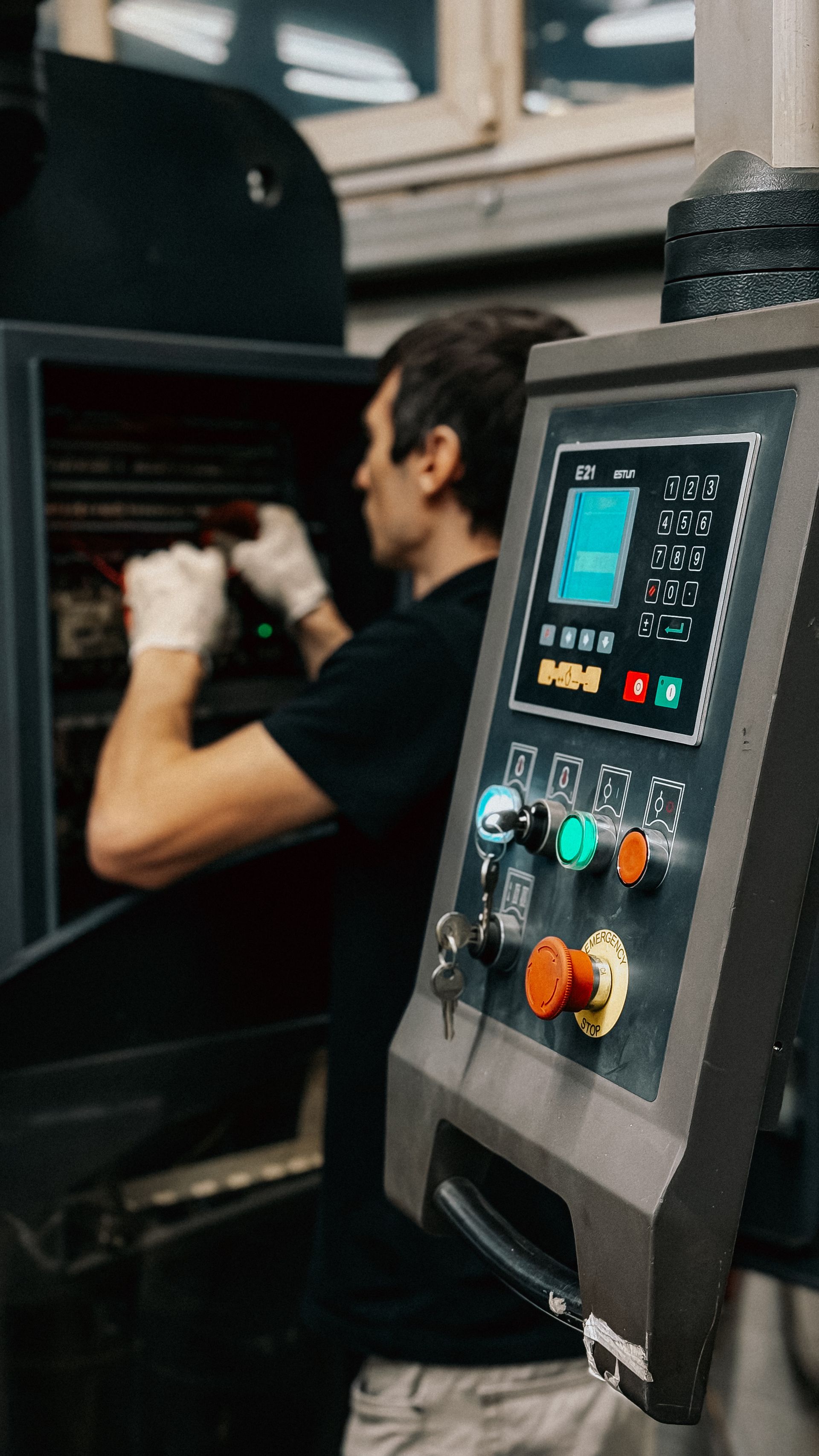Operator at a machine HMI panel while a technician works inside an open control cabinet